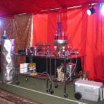 Stylish bar setup with a red draped backdrop, featuring various drink dispensers and a cooler, designed for Halloween-themed events.