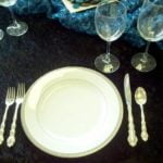 Elegant silver plate flatware setting with a dinner plate, fork, knife, and spoon, accompanied by wine glasses on a dark tablecloth, showcasing options for wedding and event rentals in Little Rock, AR.