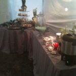 We can help plan your food/beverage and we can help you keep it hot or cold! Food service setup featuring a variety of warmers, beverage dispensers, and serving pieces on elegantly draped tables, ideal for events like weddings and parties.