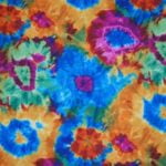 Colorful tie-dye linen featuring vibrant blue, orange, and pink floral patterns, suitable for event table settings and themed parties.