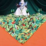 Colorful tropical-themed table linen featuring vibrant foliage and birds, layered over an orange tablecloth, ideal for event decor and themed parties.