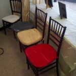 Chiavari chairs with mahogany frames and various cushion colors (black, gold, red) displayed for event rentals, showcasing options for weddings and parties.