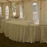 Serpentine table with white tablecloth set up in a tented event space, showcasing flexible arrangement options for gatherings and parties.