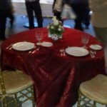 Chiavari chairs with gold finish at an elegantly set table featuring a red tablecloth, plates, and floral centerpiece, suitable for events and special occasions.