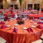 Kaleidoscope linen rental setup featuring vibrant orange tablecloths, pink napkins, and decorative centerpieces, showcasing event decor by Chris Olsen.